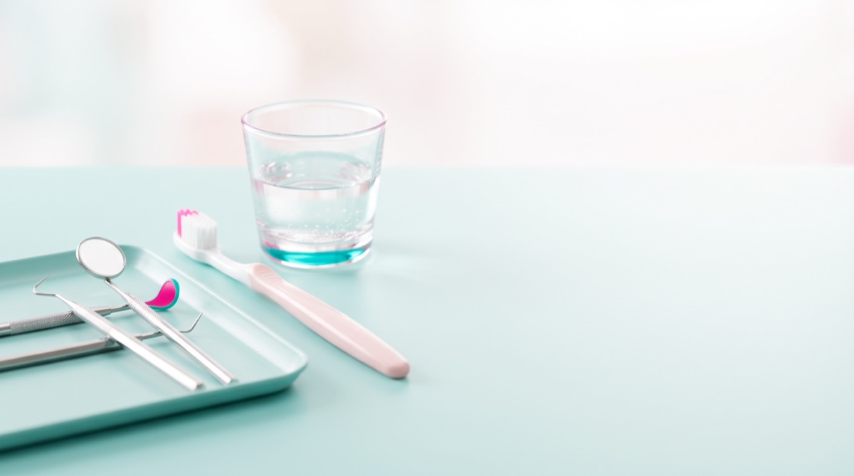 Dental mirror and explorer on a pale teal tray beside a pink toothbrush and a glass of water