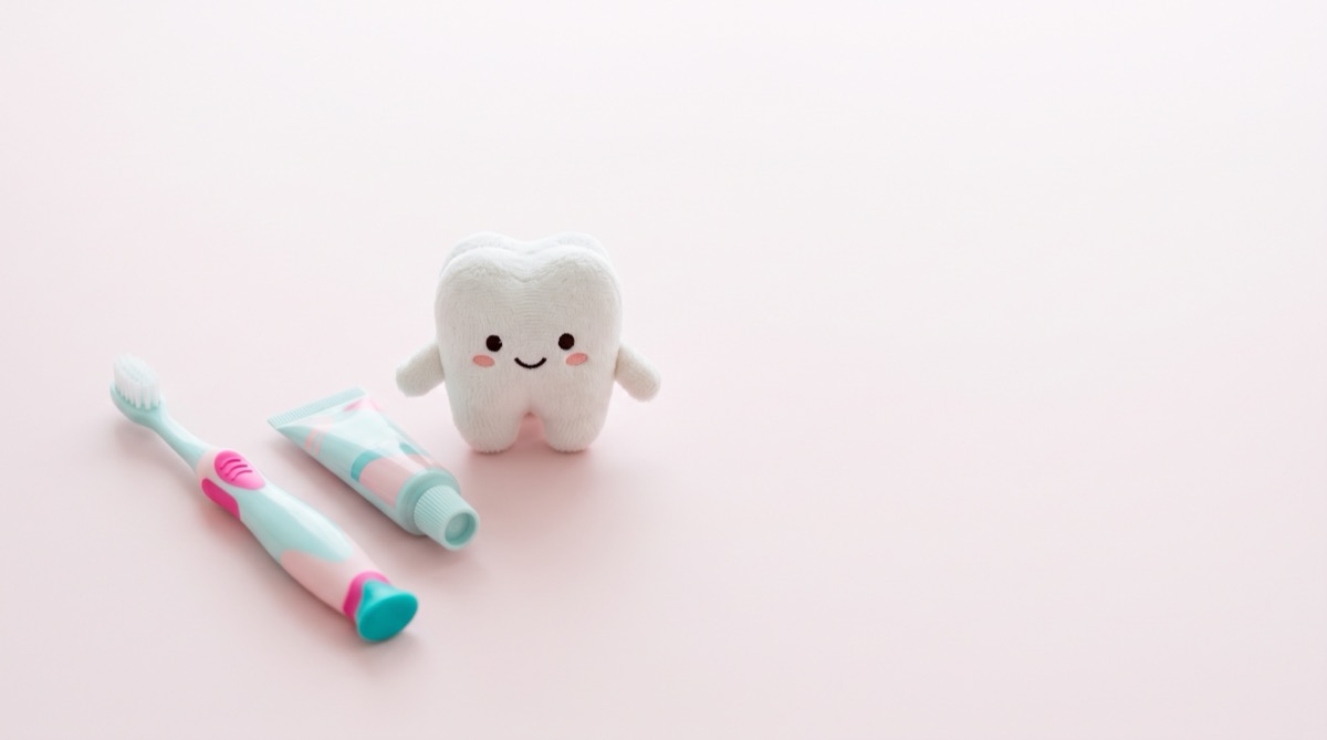 Kids' toothbrush and toothpaste beside a smiling plush tooth toy